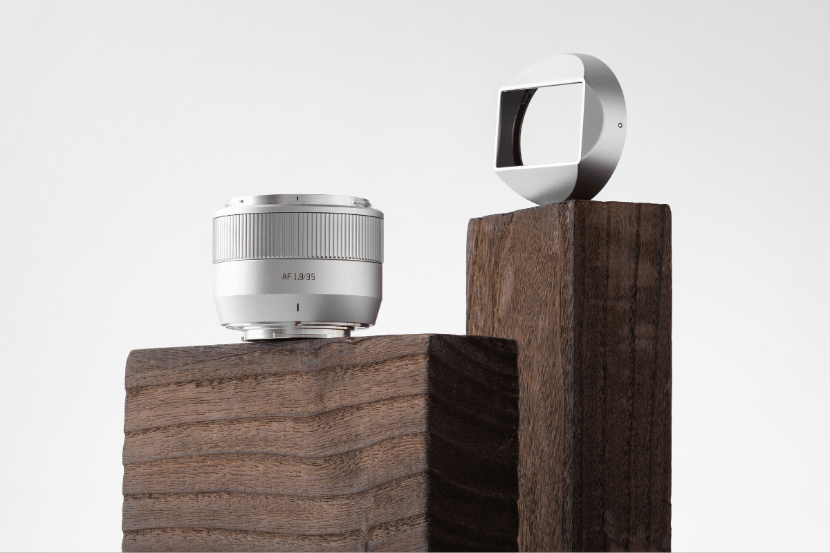Silver camera lens AF 1.8/35 and round silver camera accessory on wooden pedestals
