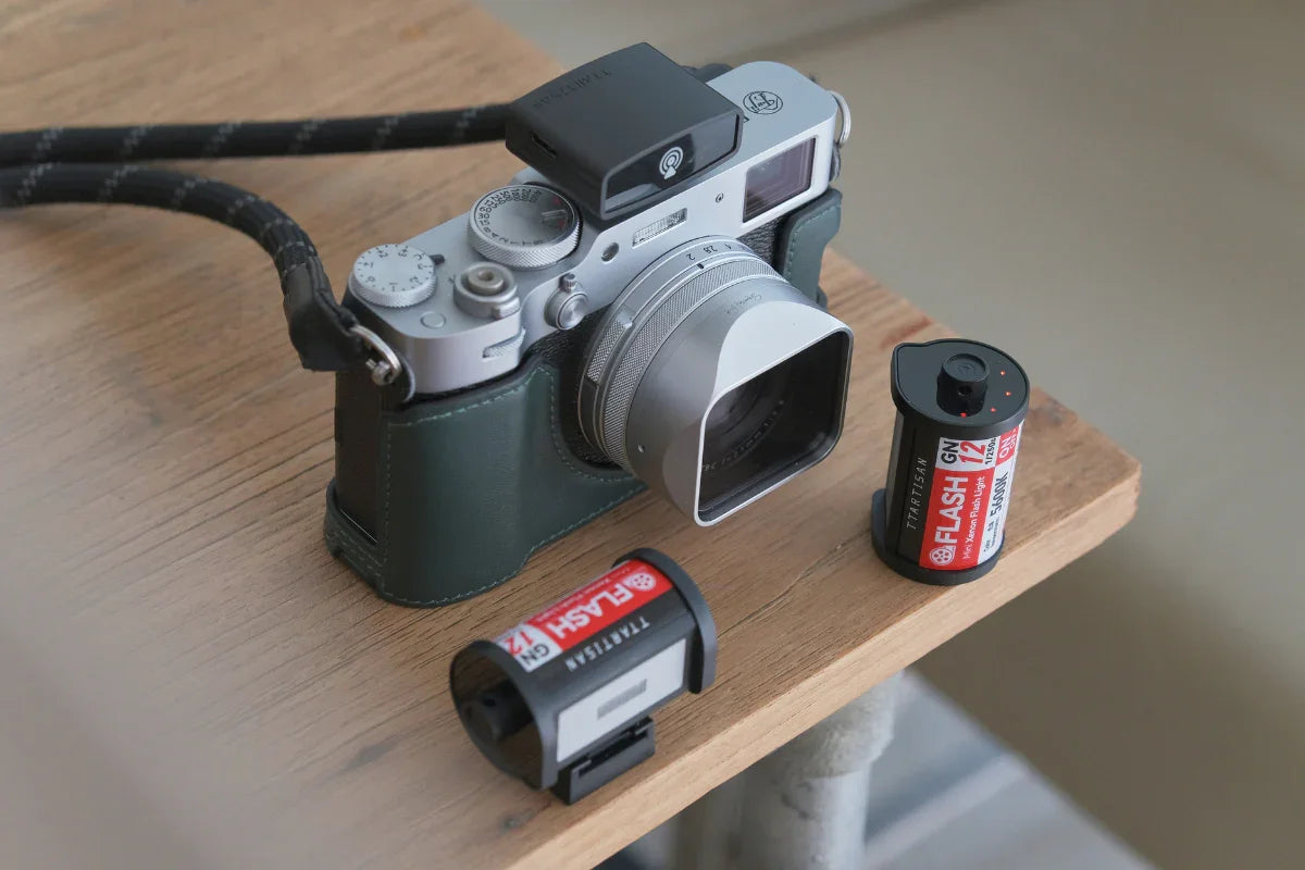 Retro-style silver camera with lens hood and two Tartisan GN12 wireless flash triggers on wooden surface