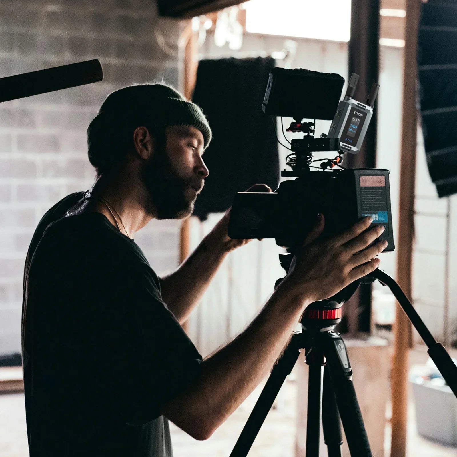Videographer adjusting professional camera on tripod in indoor studio filming setup