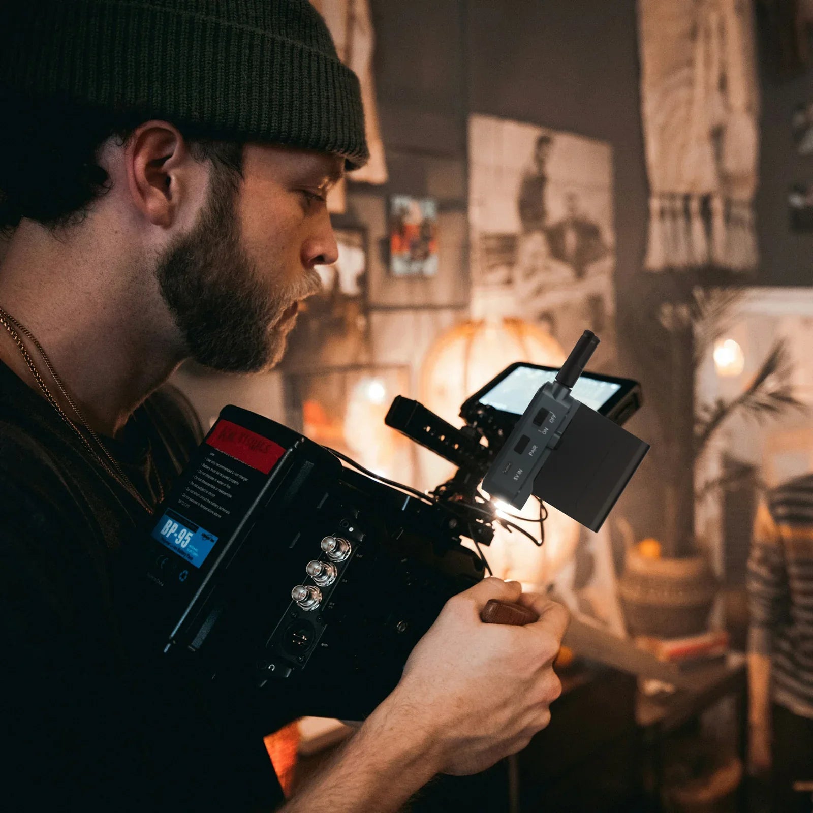 Young bearded man wearing green beanie filming indoors with professional camera and external monitor