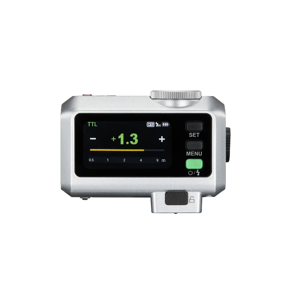 Silver camera flash remote with digital display showing TTL mode and +1.3 exposure compensation