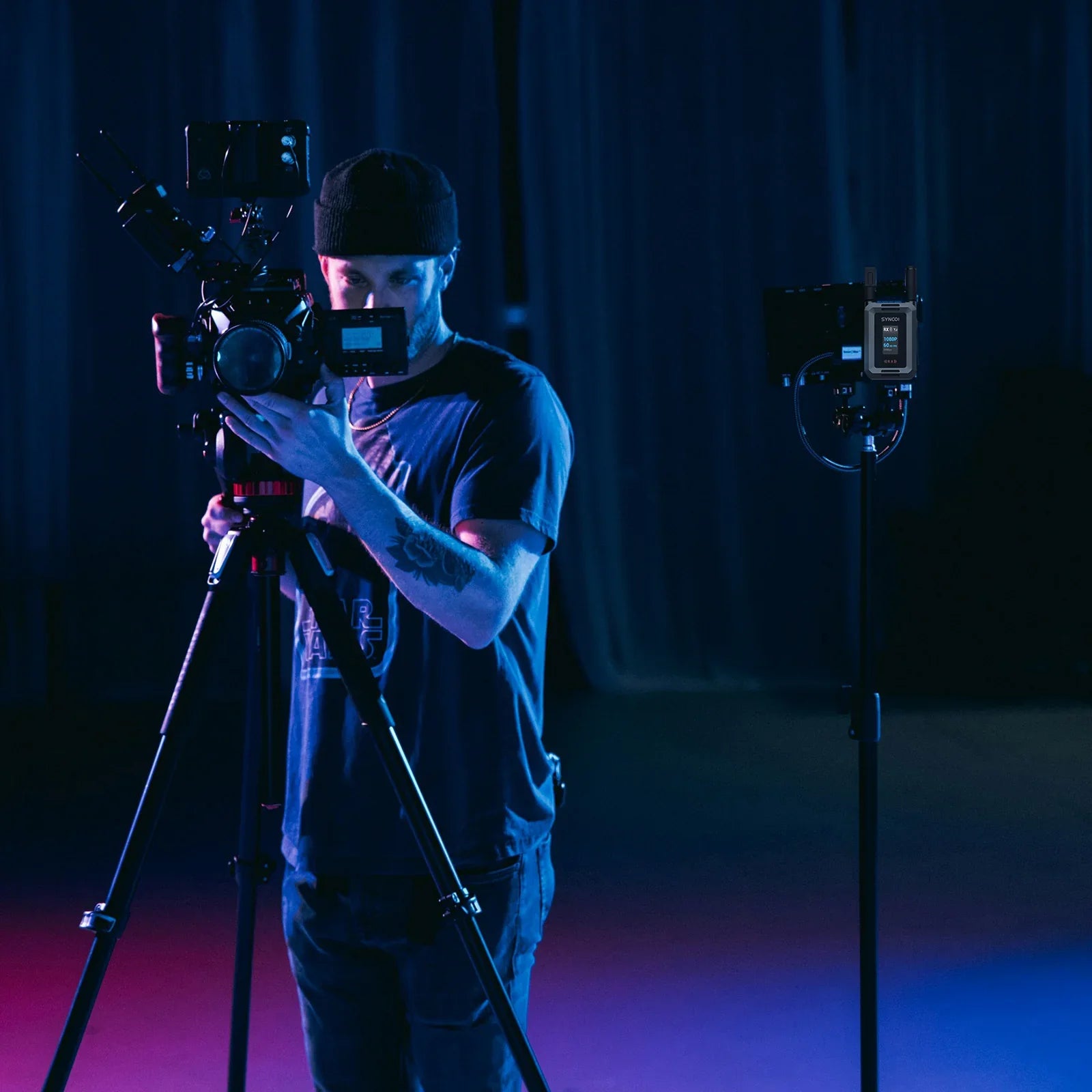 Cameraman filming with professional camera setup on tripod in dark studio with blue and purple lighting