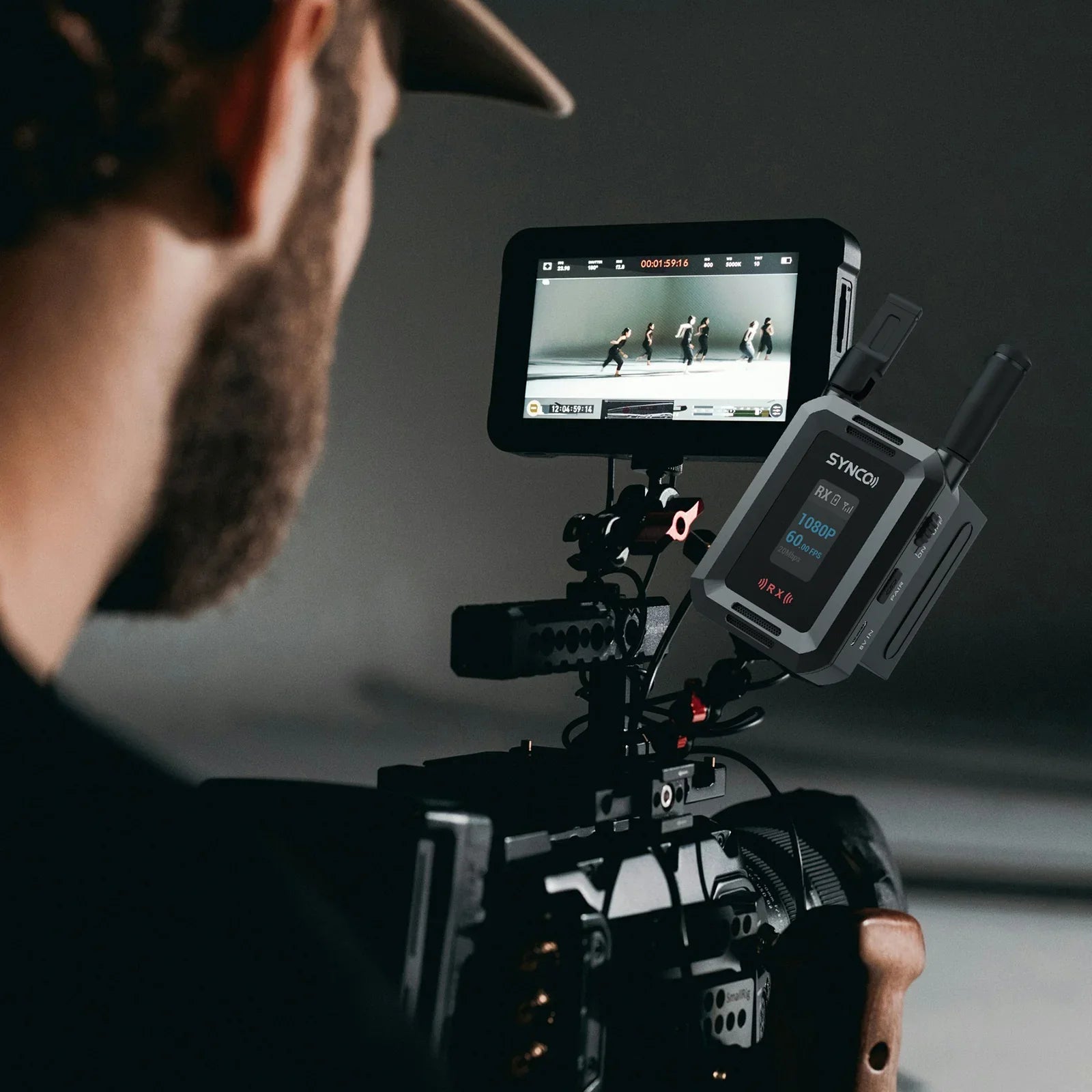 Filmmaker operating professional video camera with attached SYNCO wireless receiver and external monitor showing dancers
