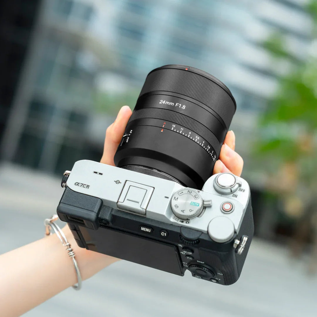 Person holding Sony Alpha 7C II camera with 24mm F1.8 lens outdoors in urban setting