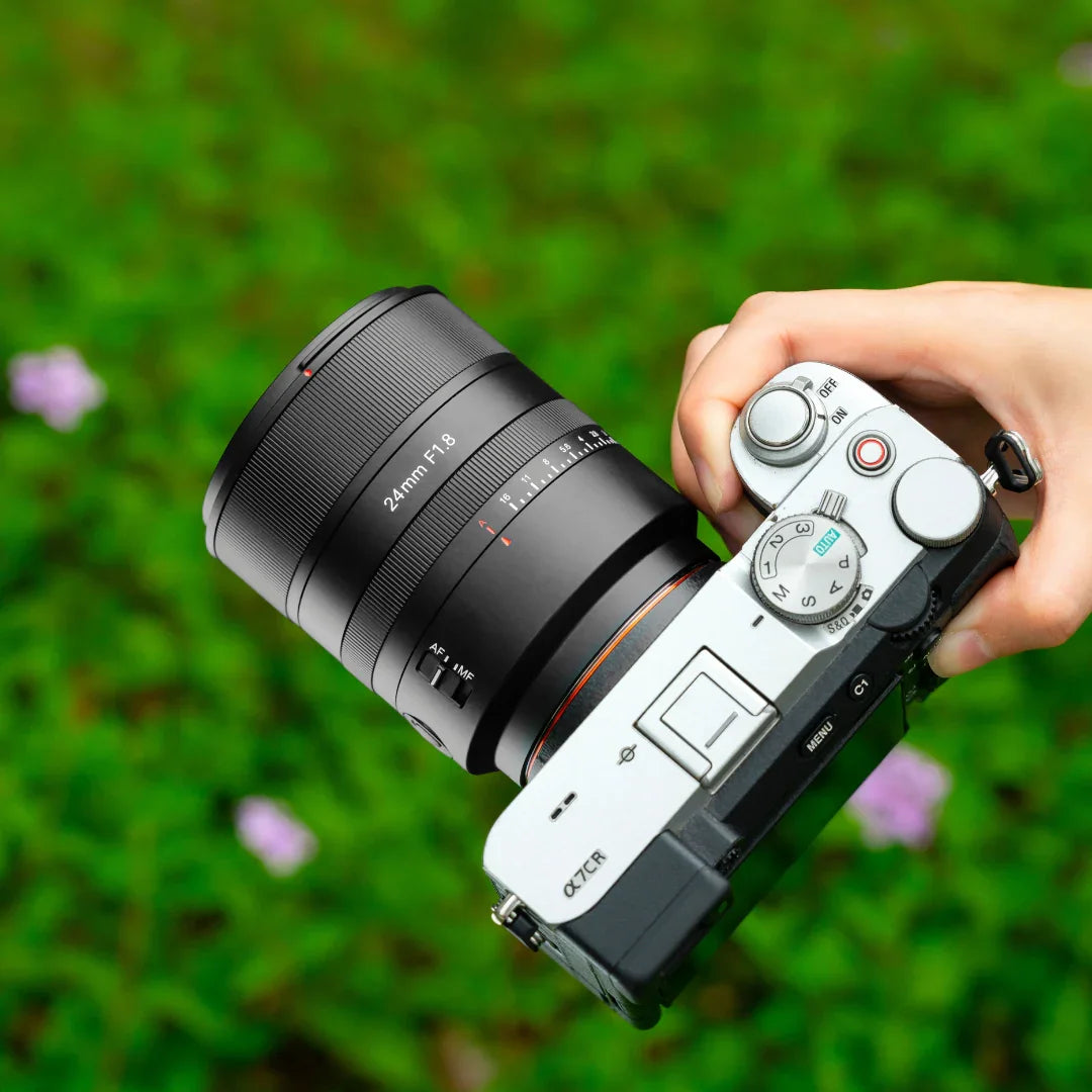 Hand holding Sony Alpha 7CR camera with 24mm F1.8 lens against green blurred background