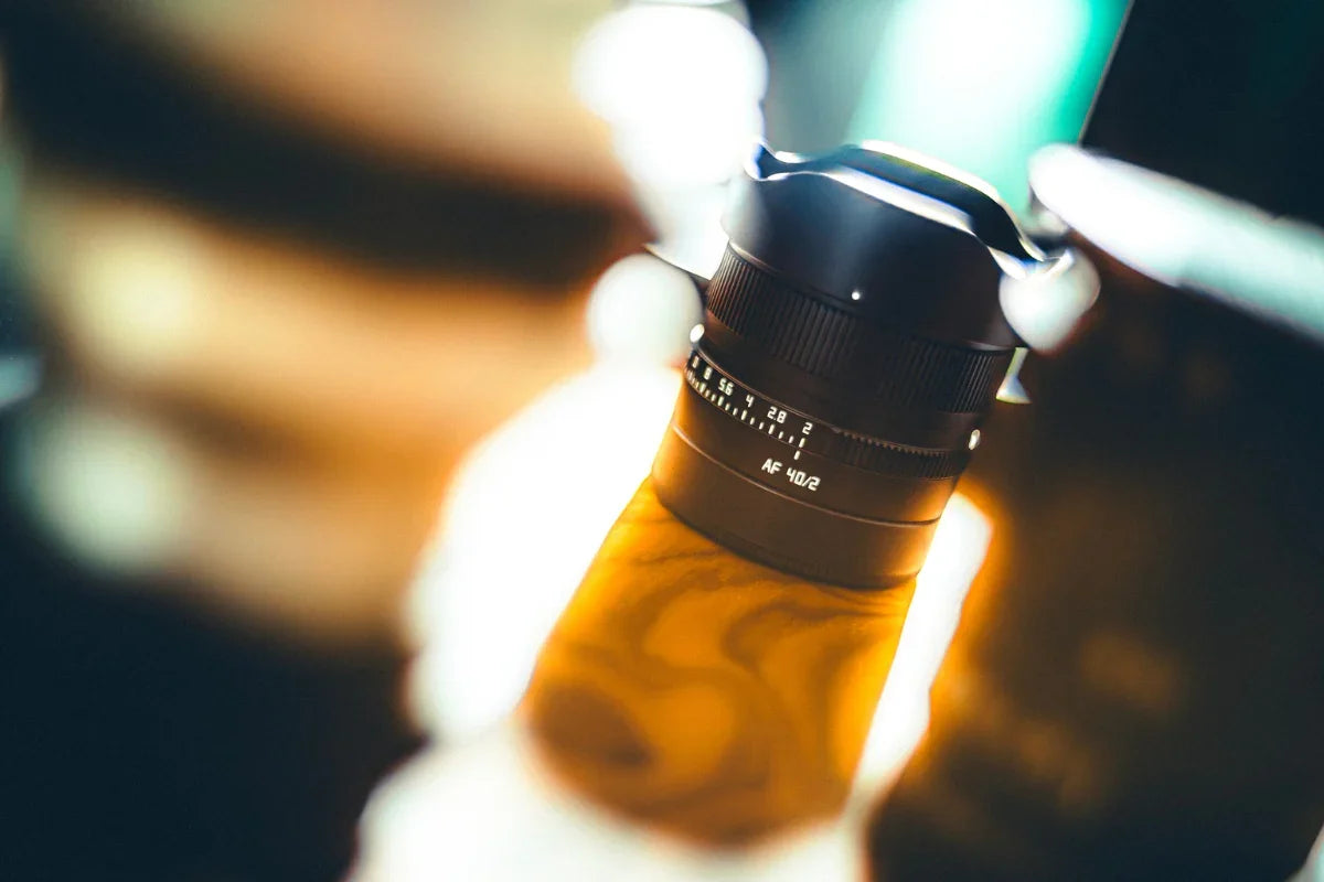 Black AF 40/2 camera lens on a wooden surface with blurred lights in background